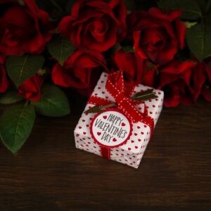 Valentine's Day background with red roses and a gift on a rustic wood table
